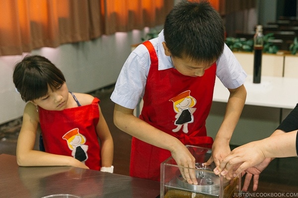 children pressing weight on fabric soaked in soy sauce at Kikkoman Factory in Noda Japan | justonecookbook.com