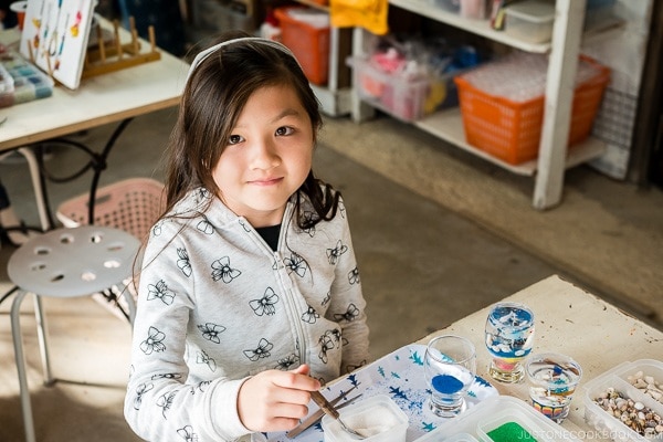 child looking at camera sitting in front of art craft at Ryukyu Mura Okinawa | justonecookbook.com