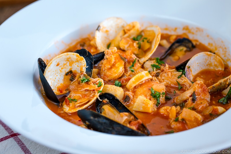 A white bowl containing Cioppino (Seafood Stew) served with rustic bread.