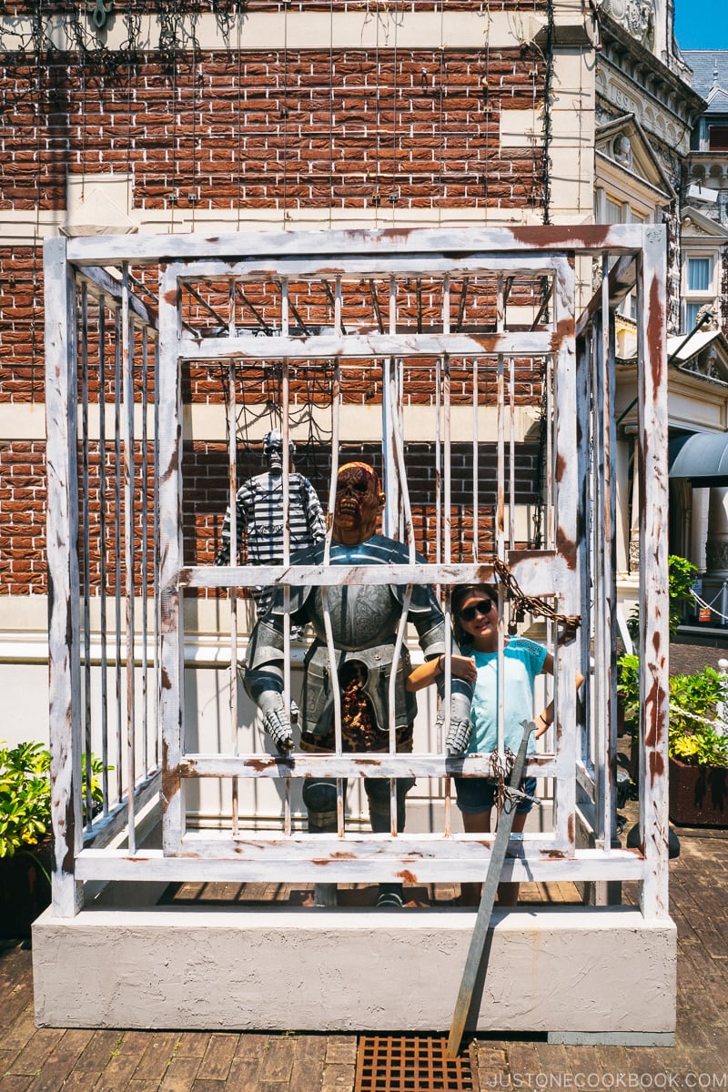 girl with model of a scary creature behind bars