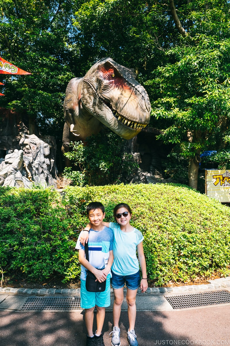 two children in front of mechanical dinosaur inside trees