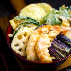 Assorted tempura served on a bed of steamed rice in a red lacquered bowl.