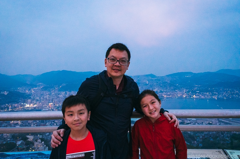 man with two children with city of Nagasaki in the background