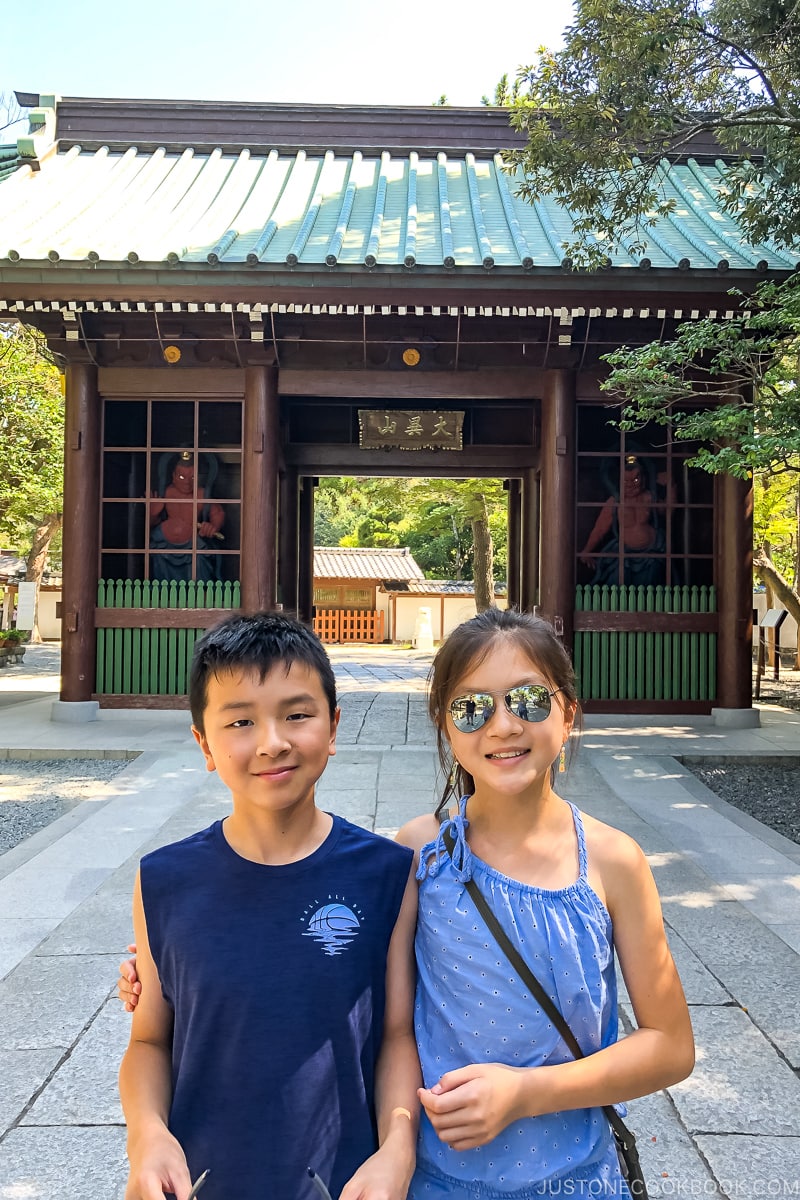 two children standing on a stone path in front of temple gate