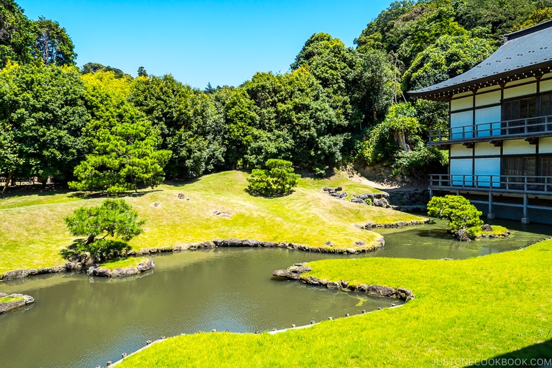 a garden with a green grass and small pond in the center and trees in the back next to a temple