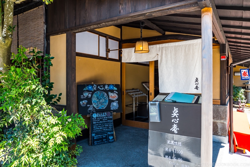 entrance to a restaurant with white curtains and signs in front