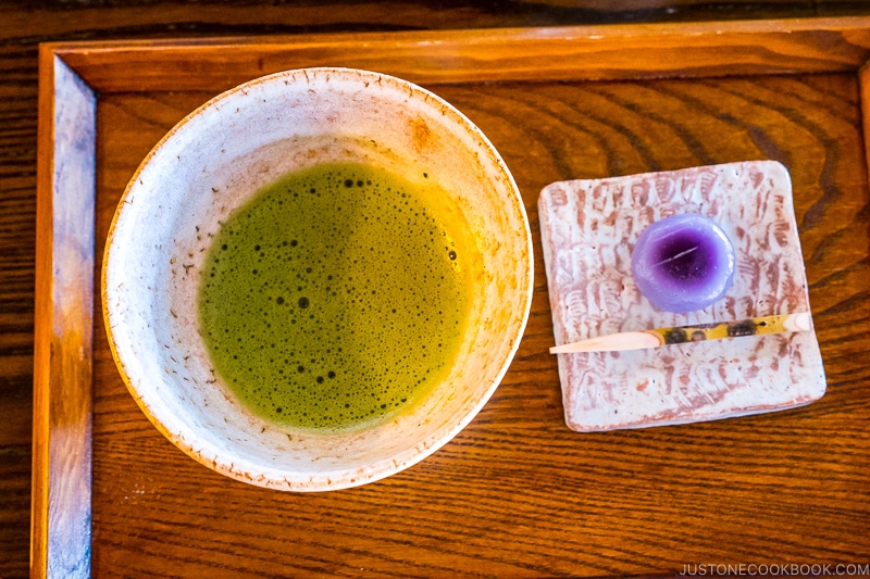 a wooden tray with matcha green tea on in a bowl on the left and sweets on the right