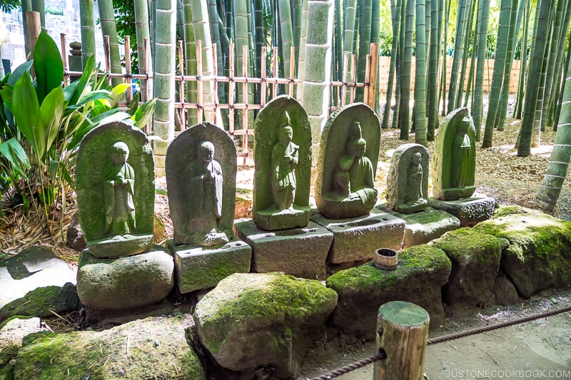 stone statue of deities on stone pedestal in front of bamboo garden