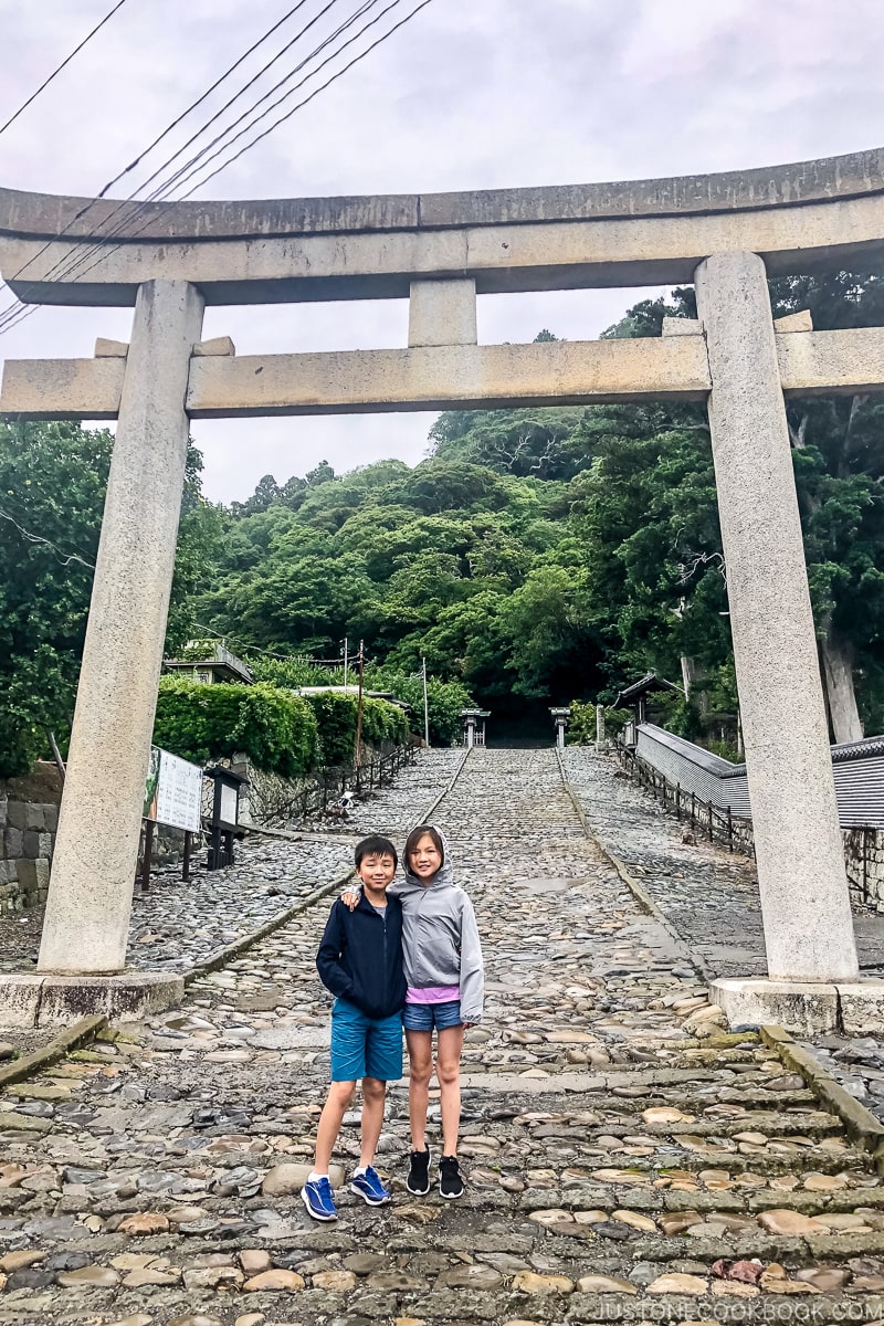 two children standing under a large stone torii gate