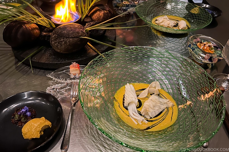 squid shaped coconut strips next to shaved celery roots in curry sauce in a glass bowl