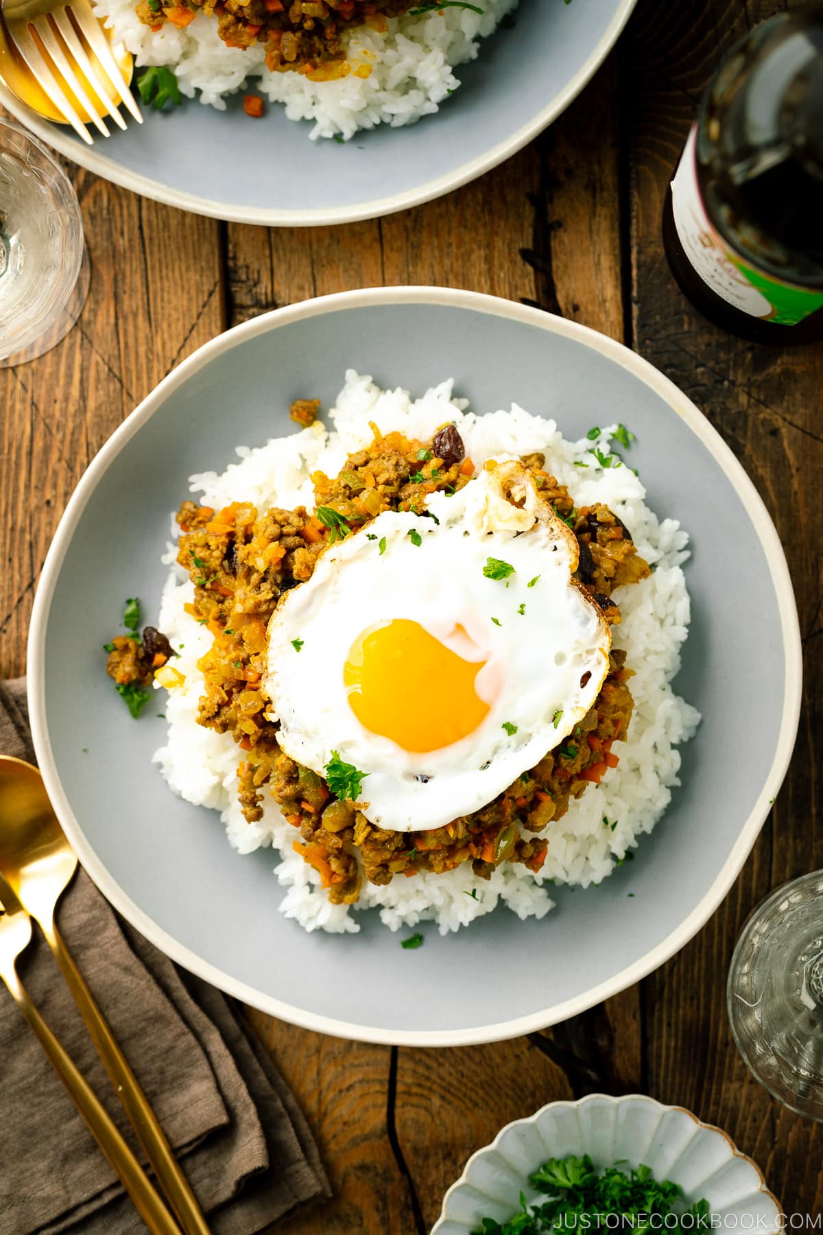 A ceramic plate containing steamed rice, dry curry, and a fried egg.