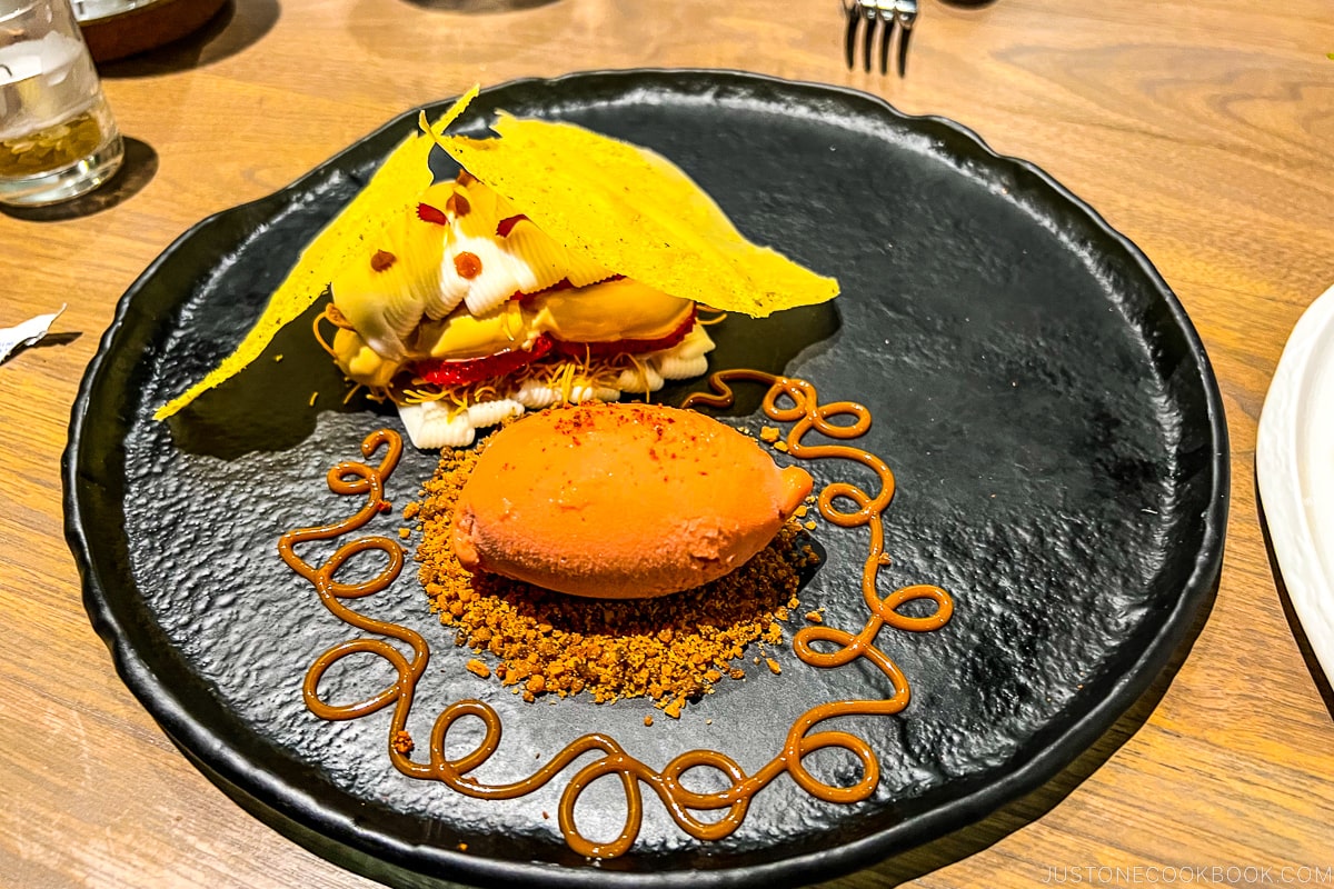 Strawberry-mint-lime sorbet, coconut praline, coconut-rum custard, phyllo dough with pistachio dust, strawberries, dulce de leche foam, crispy kataifi on a dark plate