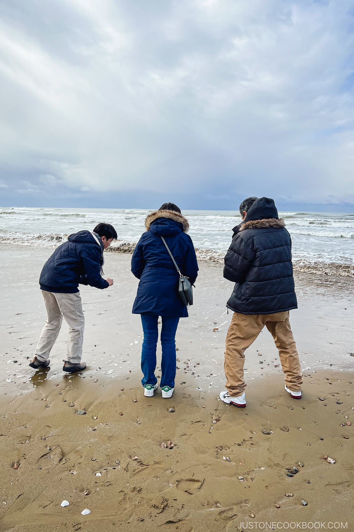 three people facing the ocean wave