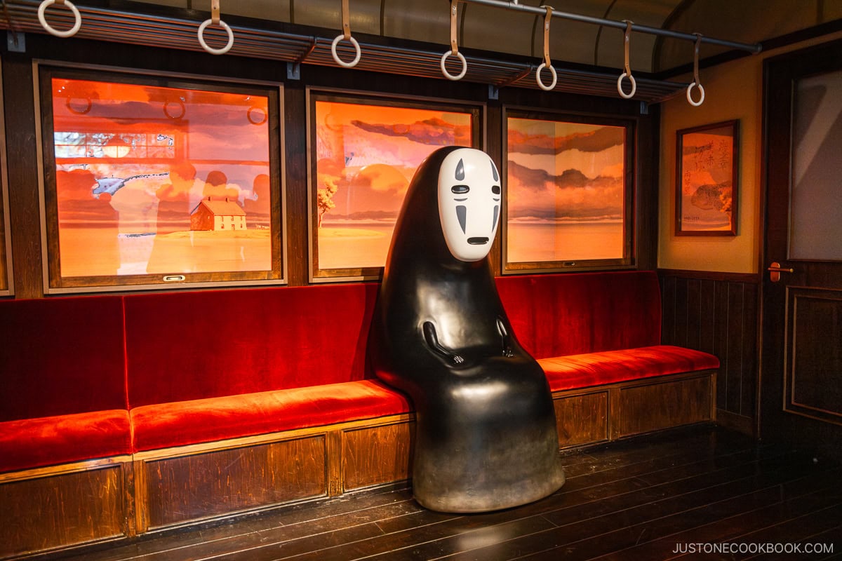 No Face character from Spirited Away sitting on a train