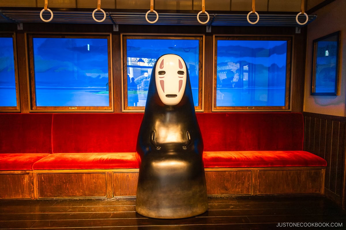 No Face character from Spirited Away sitting on a train