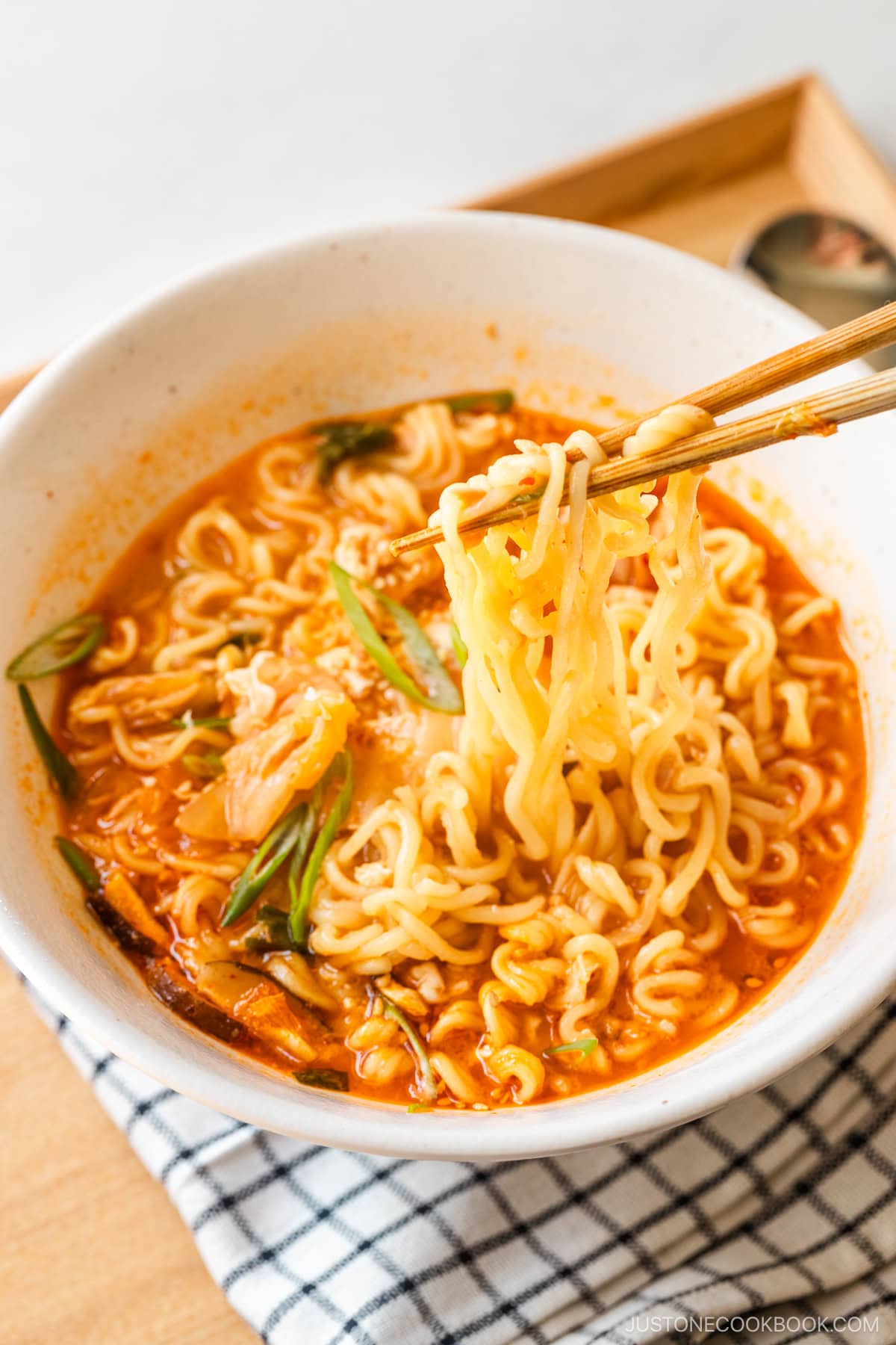 A white ramen bowl containing Korean ramen (ramyeon), topped with soft-cooked egg, kimchi, and green onions.