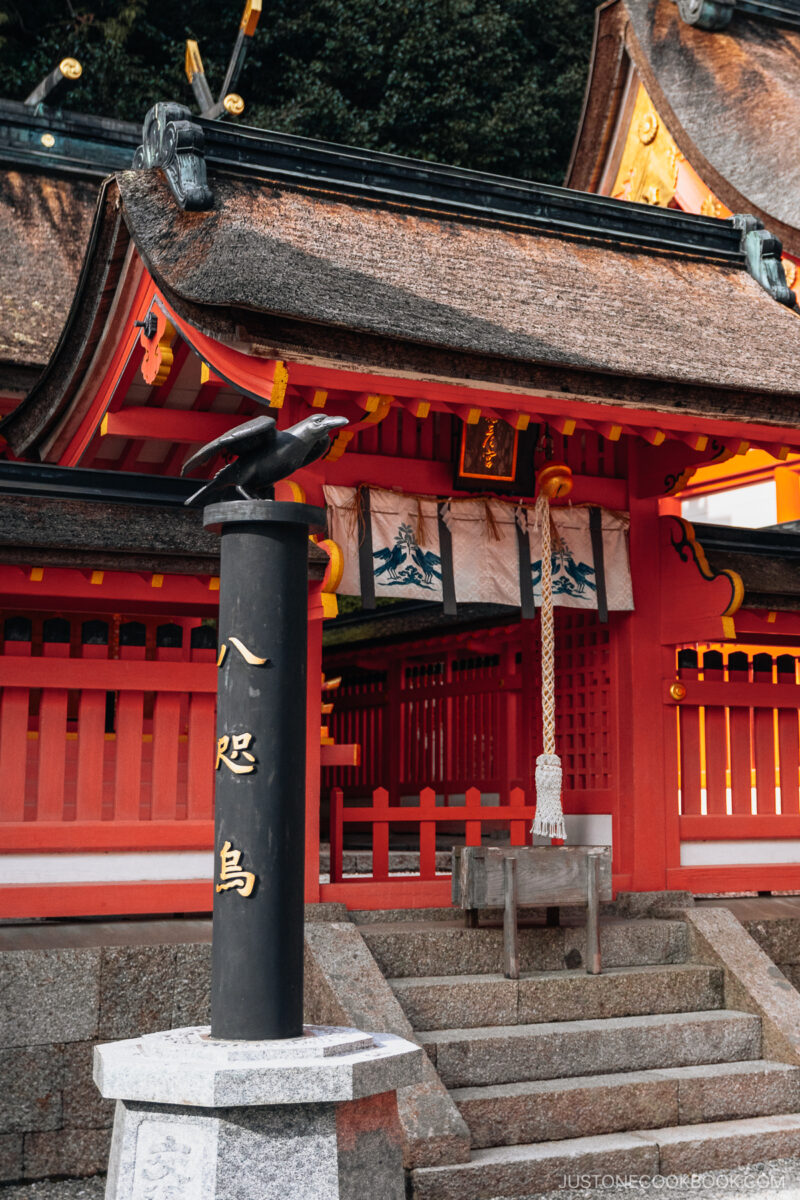 Black three legged crow statue with shrine in the background