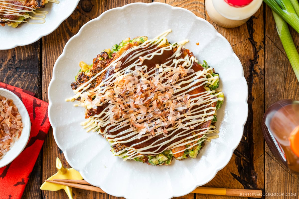 A white fluted plate containing Negiyaki, Japanese scallion okonomiyaki, drizzled with okonomi sauce and Japanese Kewpie mayo.