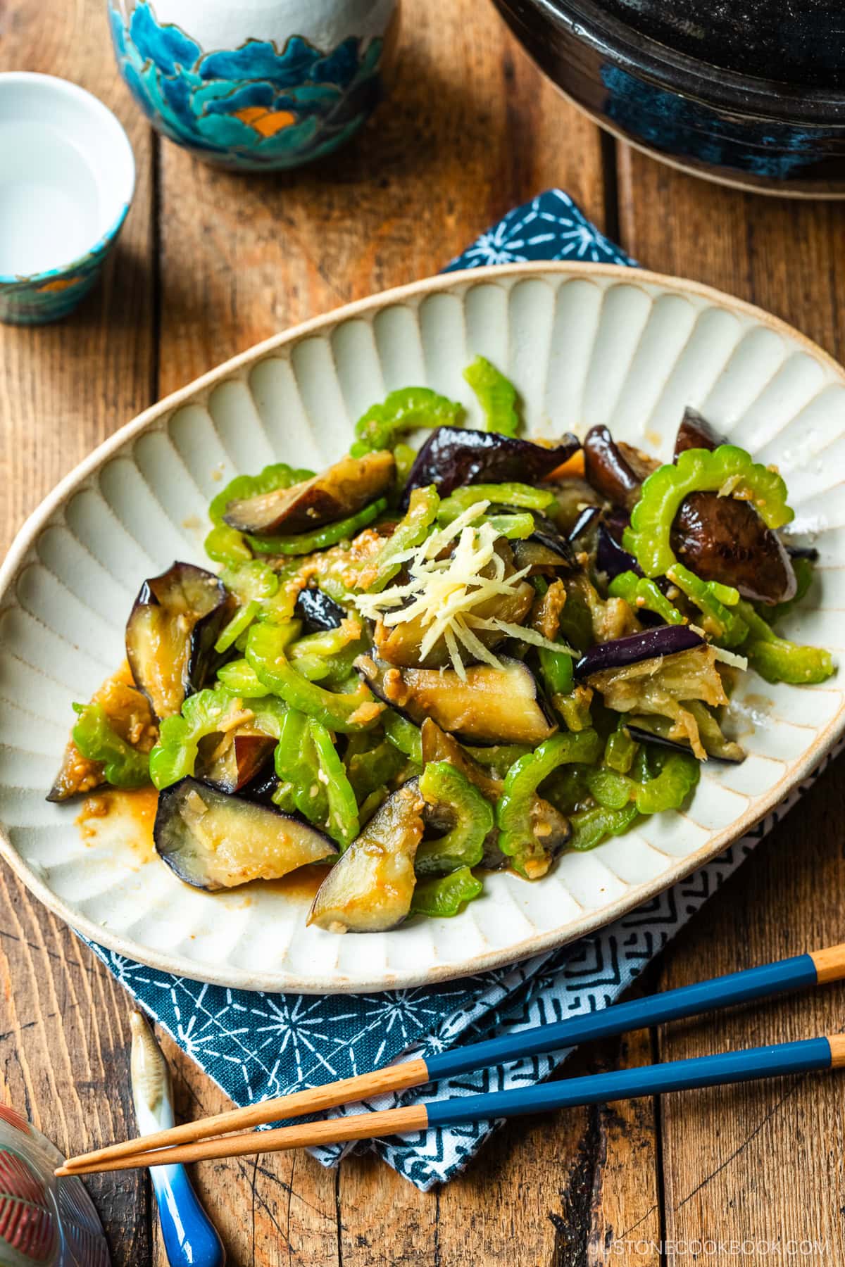 An oval fluted plate containing Stir-Fried Bitter Melon and Eggplant topped with julienned ginger.