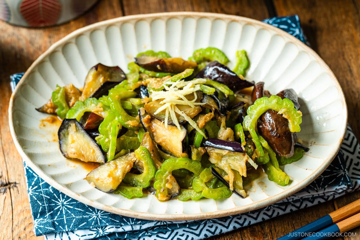 An oval fluted plate containing Stir-Fried Bitter Melon and Eggplant topped with julienned ginger.