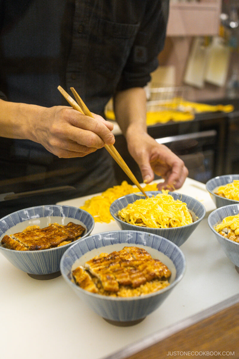 Chef adding sliced egg on top of unagi