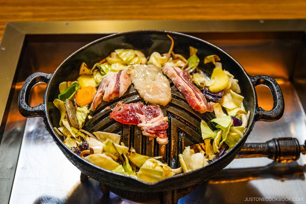 Lamb and vegetables being grilled on a dome-shaped grill