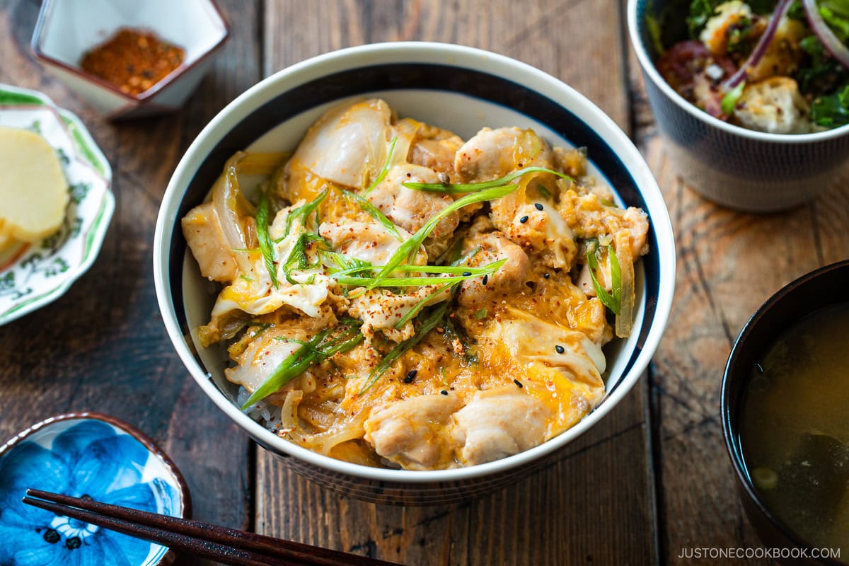A Japanese ceramic bowl containing Oyakodon, a chicken and egg rice bowl dish garnish with green onion.