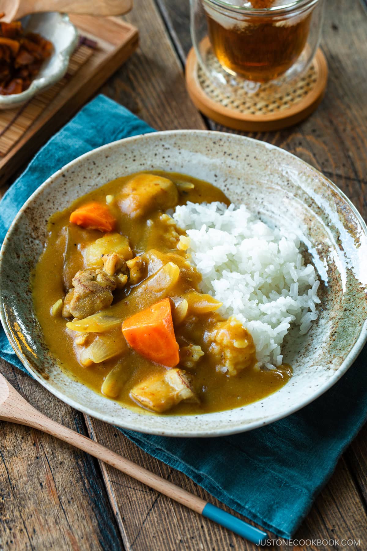 A round plate containing Japanese chicken curry over steamed rice, garnished with fukujinzuke pickles.