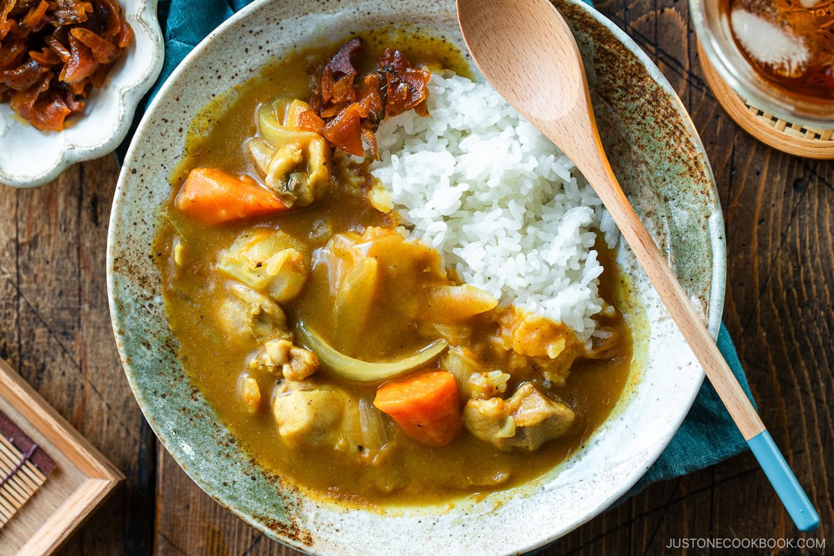 A round plate containing Japanese chicken curry over steamed rice, garnished with fukujinzuke pickles.