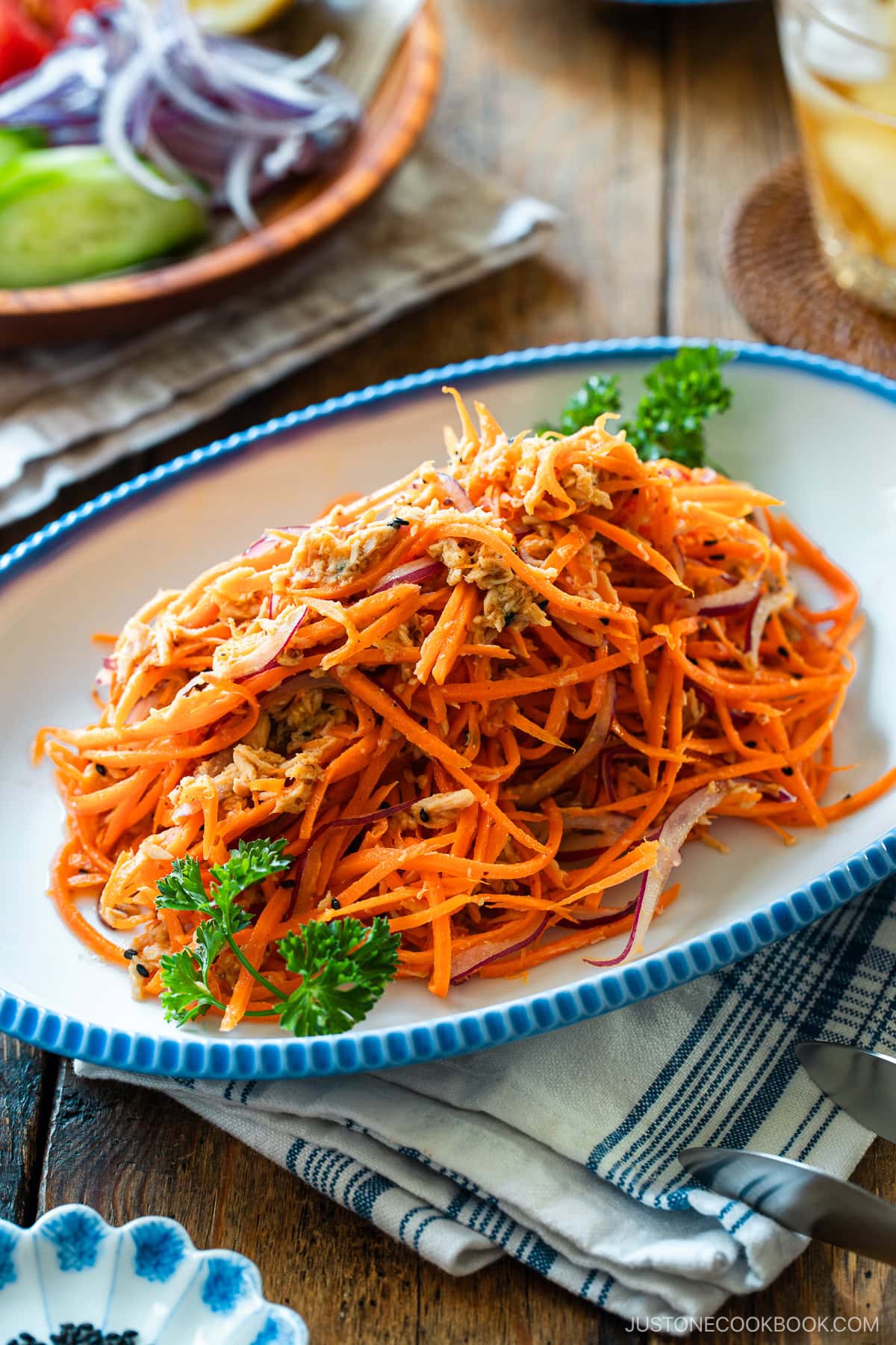 An oval scalloped plate containing shredded carrot and tuna salad garnished with parsley and lemon.