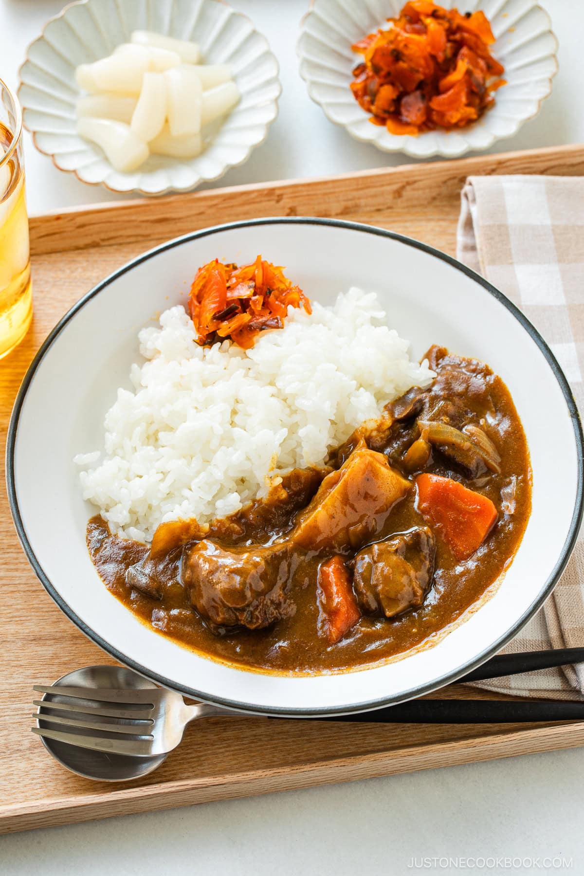 A round white plate containing Japanese beef curry consisting of tender beef, potatoes, carrots, mushrooms, and curry roux, served over steamed rice.