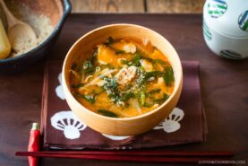 A light wooden bowl containing Spicy Pork and Bean Sprout Miso Soup sprinkled with ground sesame seeds.