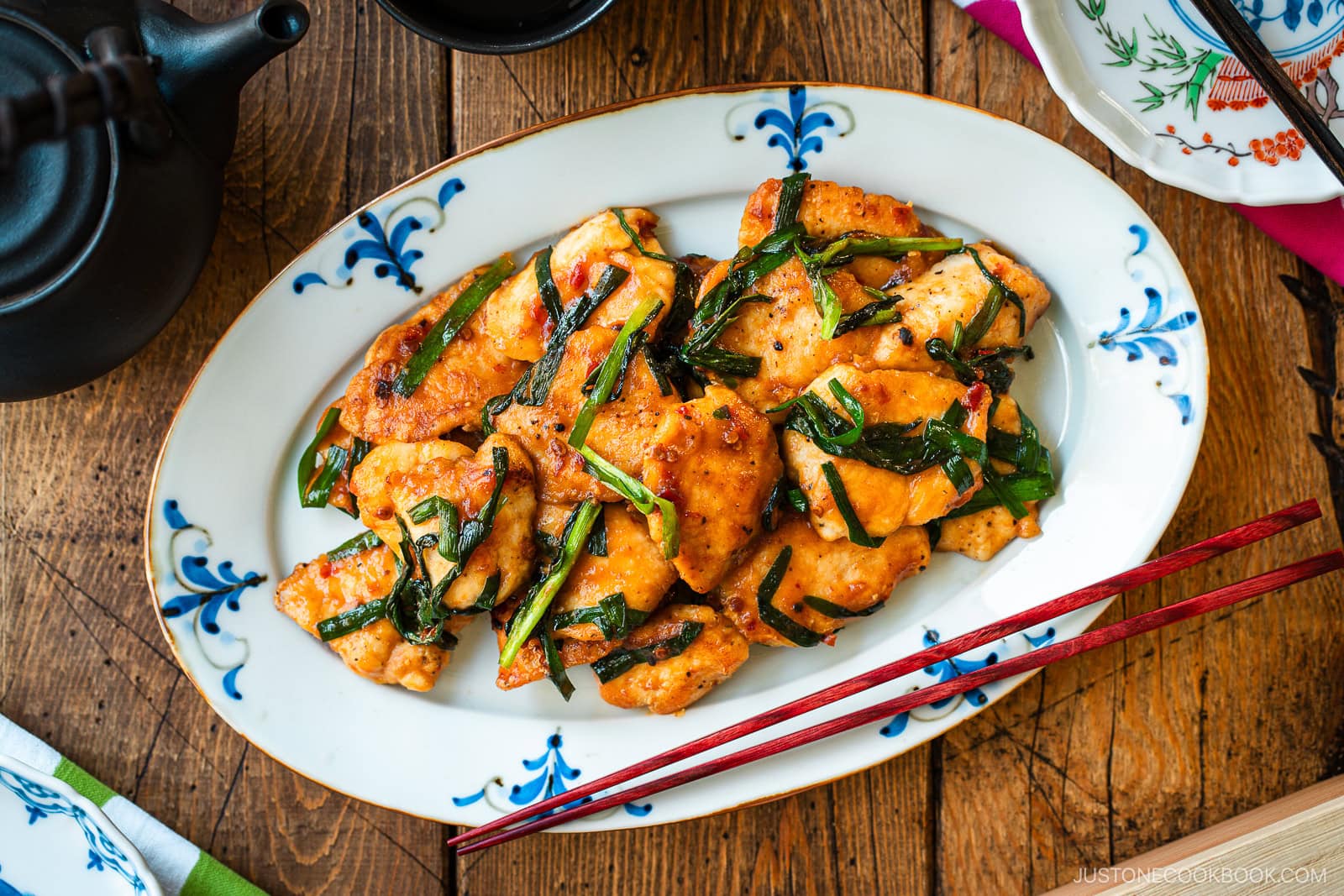 An oval plate containing Chicken Stir-fry with Garlic Chives served on the table along with tea pot and small plates.