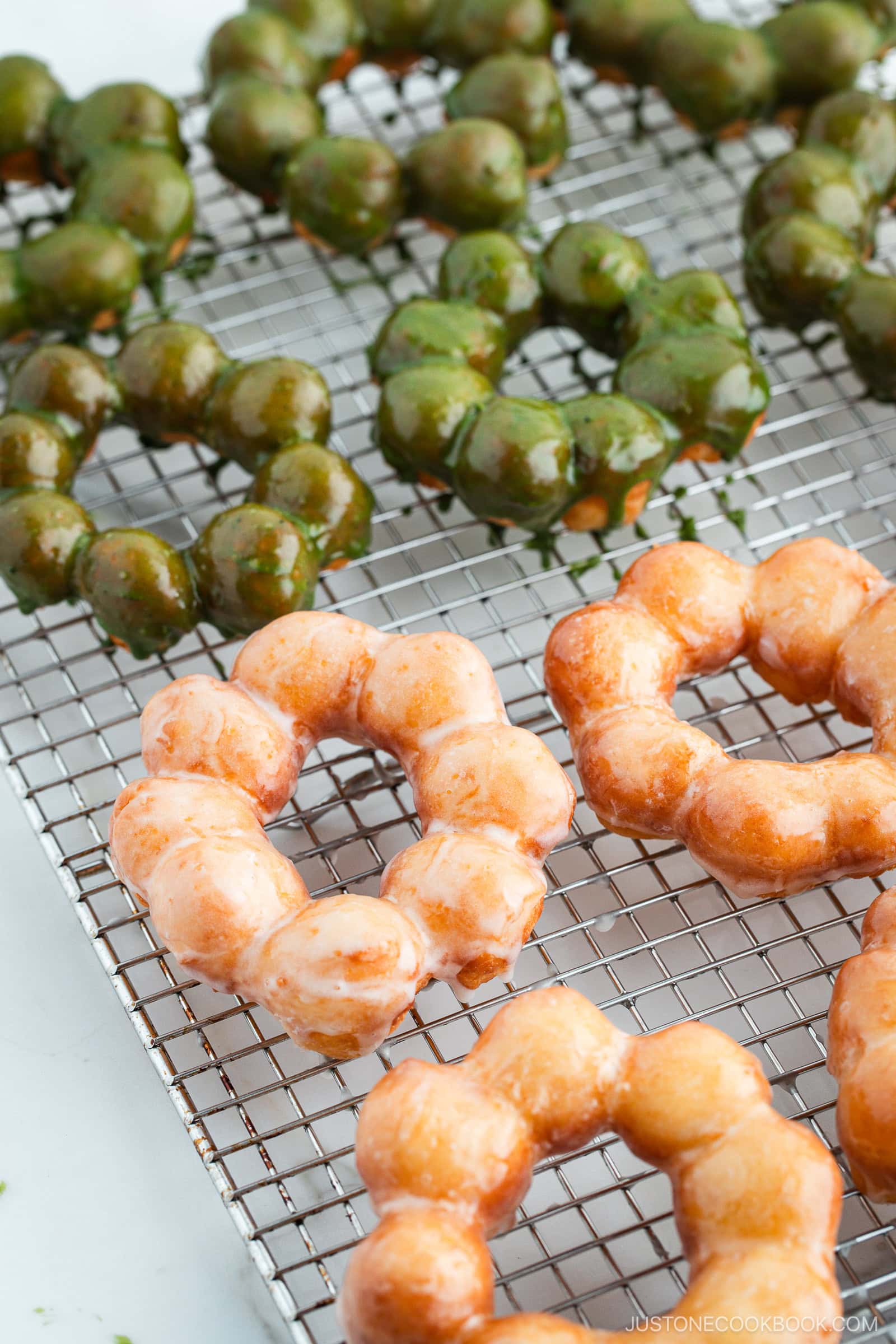 Copycat Pon de Ring donuts, hot from the fryer and still glistening with sugar and matcha glaze, cooling on a wire rack.