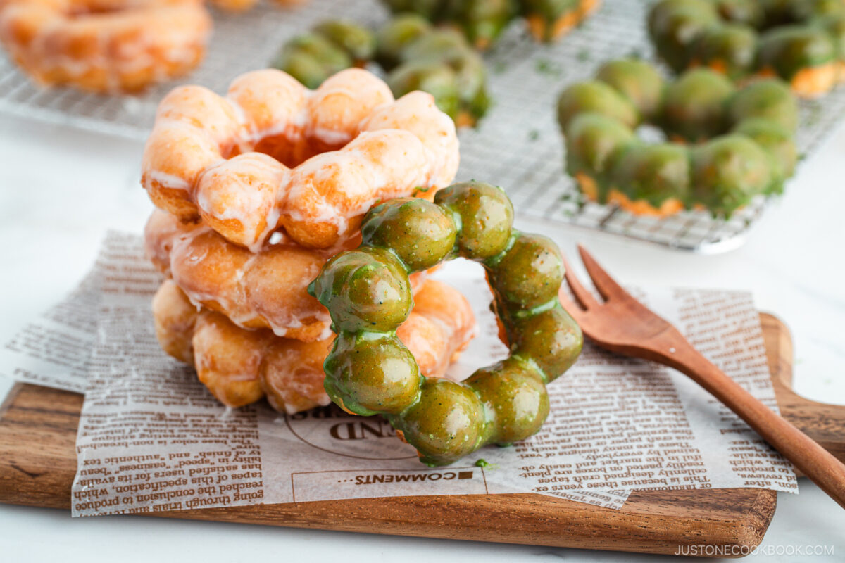 Copycat Pon de Ring donuts, hot from the fryer and still glistening with sugar and matcha glaze, stacked atop one another on a rustic wooden board.