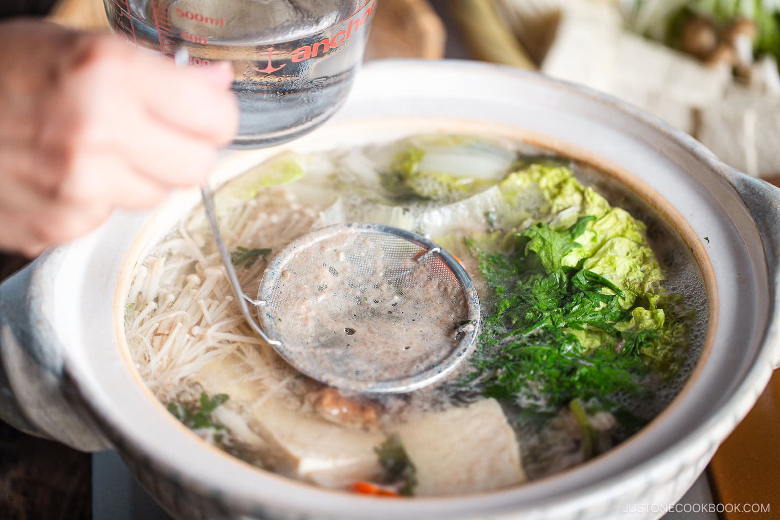 Skimming scum with a fine mesh skimmer in a donabe, Japanese hot pot.