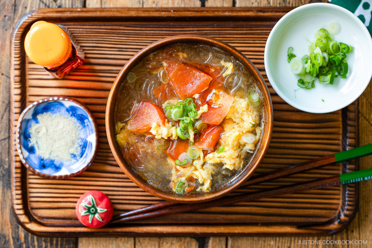 A wooden bowl containing tomato egg vermicelli soup garnished with green onion.
