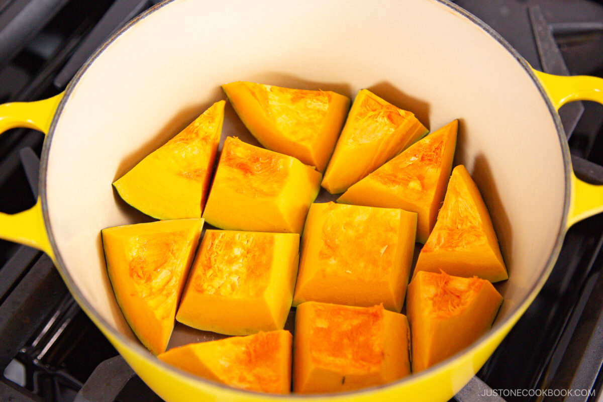 Yellow pot filled with cut pieces of bright orange kabocha squash, arranged in a single layer and ready for cooking on a stovetop.