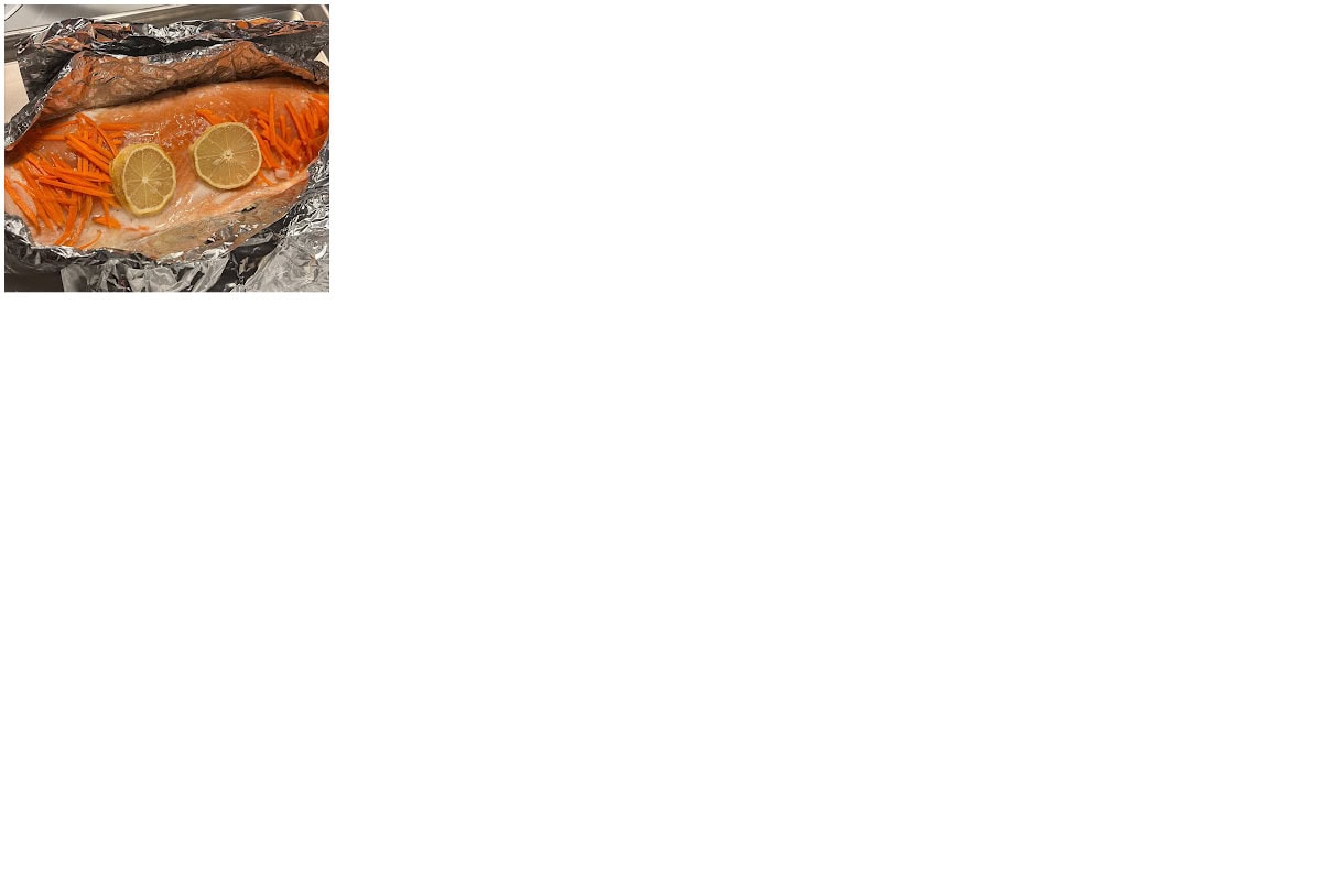 A fillet of salmon in aluminum foil topped with two lemon slices and surrounded by strips of carrot, ready to be cooked.