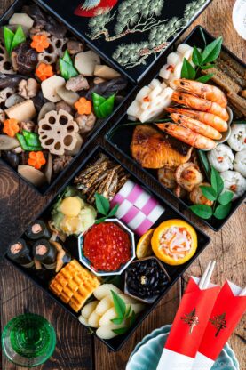 A traditional Japanese New Year’s feast (osechi ryori) in elegant black lacquer boxes, featuring assorted seafood, vegetables, rolled omelet, pickled dishes, and decorative garnishes, set on a wooden table with chopsticks.