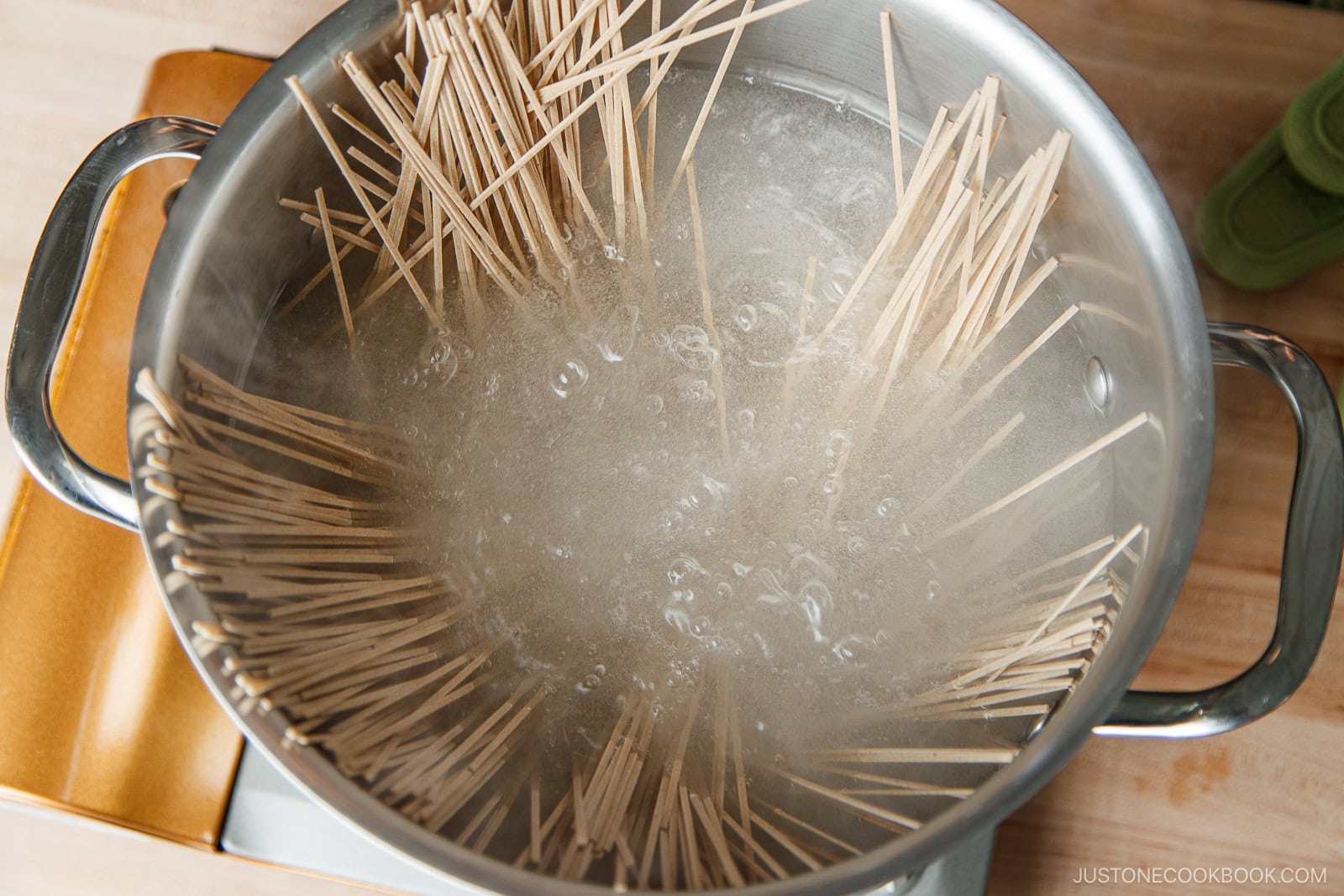 A pot of boiling water with uncooked spaghetti partially submerged, with some noodles still sticking out above the water. The pot is on a stovetop.