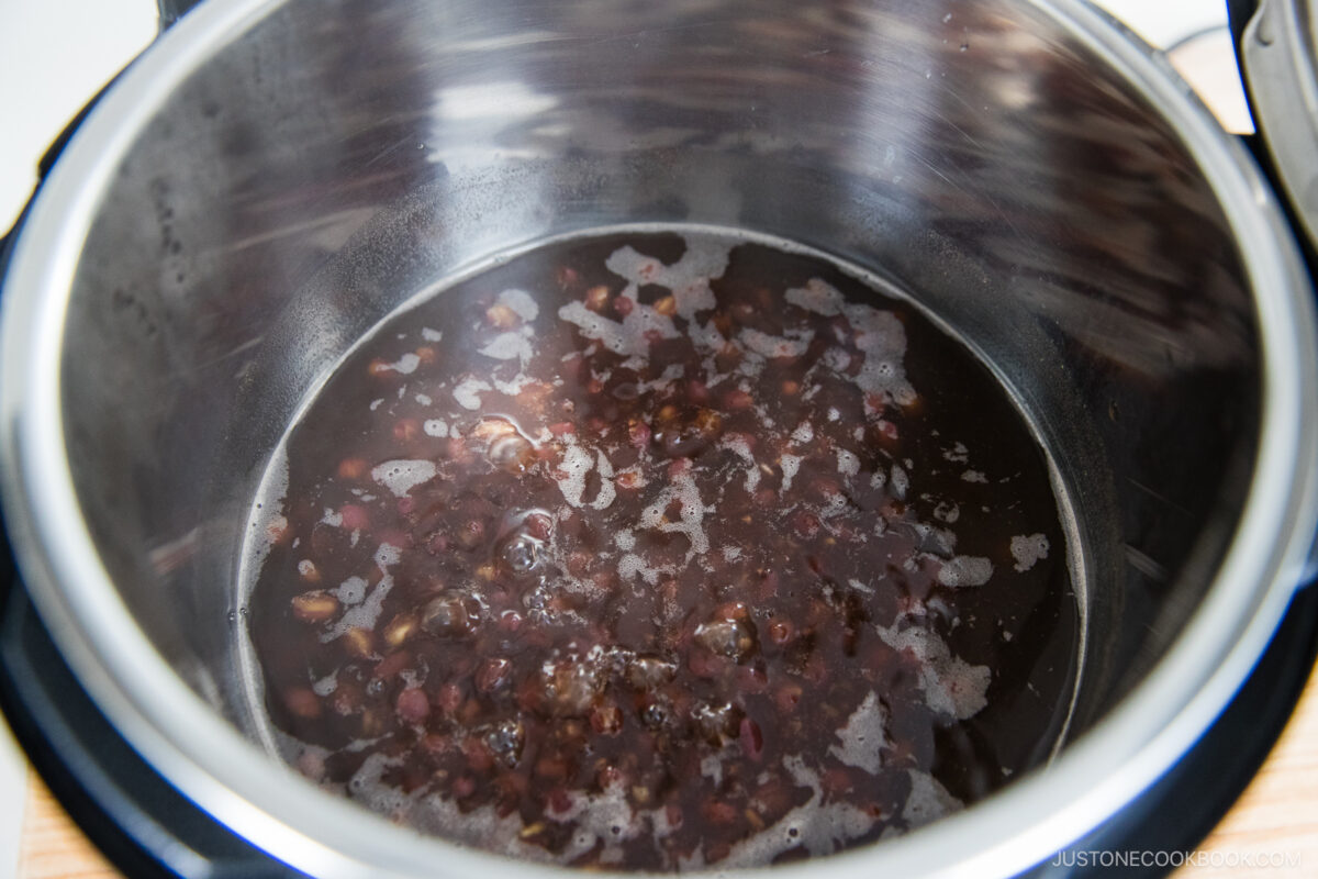 A close-up view of cooked red beans in a liquid inside a stainless steel pot, with some steam rising and condensation on the pot’s sides.