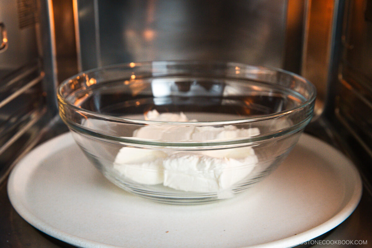 A glass bowl with blocks of cream cheese sits on a microwave turntable, ready to be heated for a delicious Basque cheesecake.