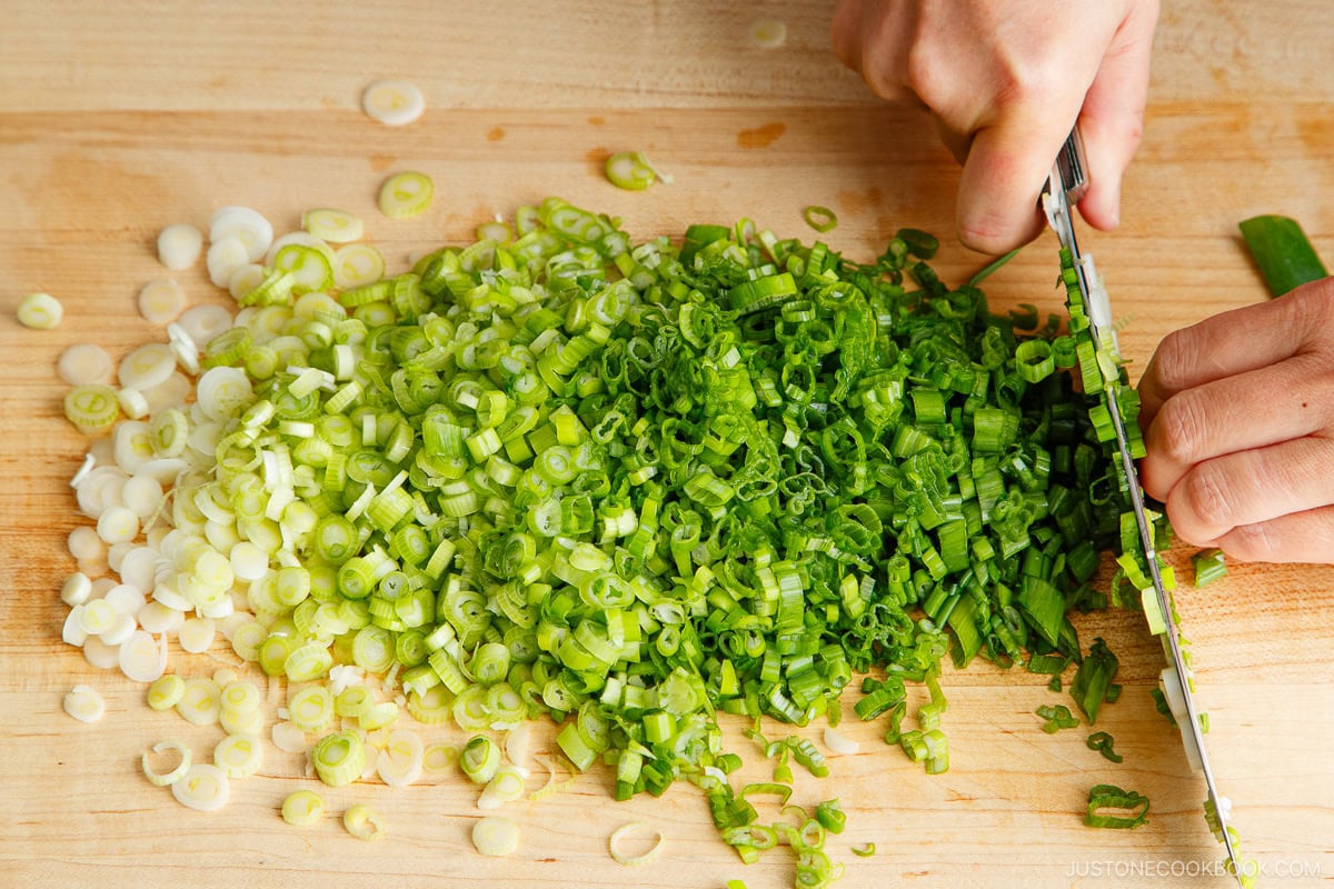 A large pile of sliced green onions cut with a kitchen knife on a cutting board.