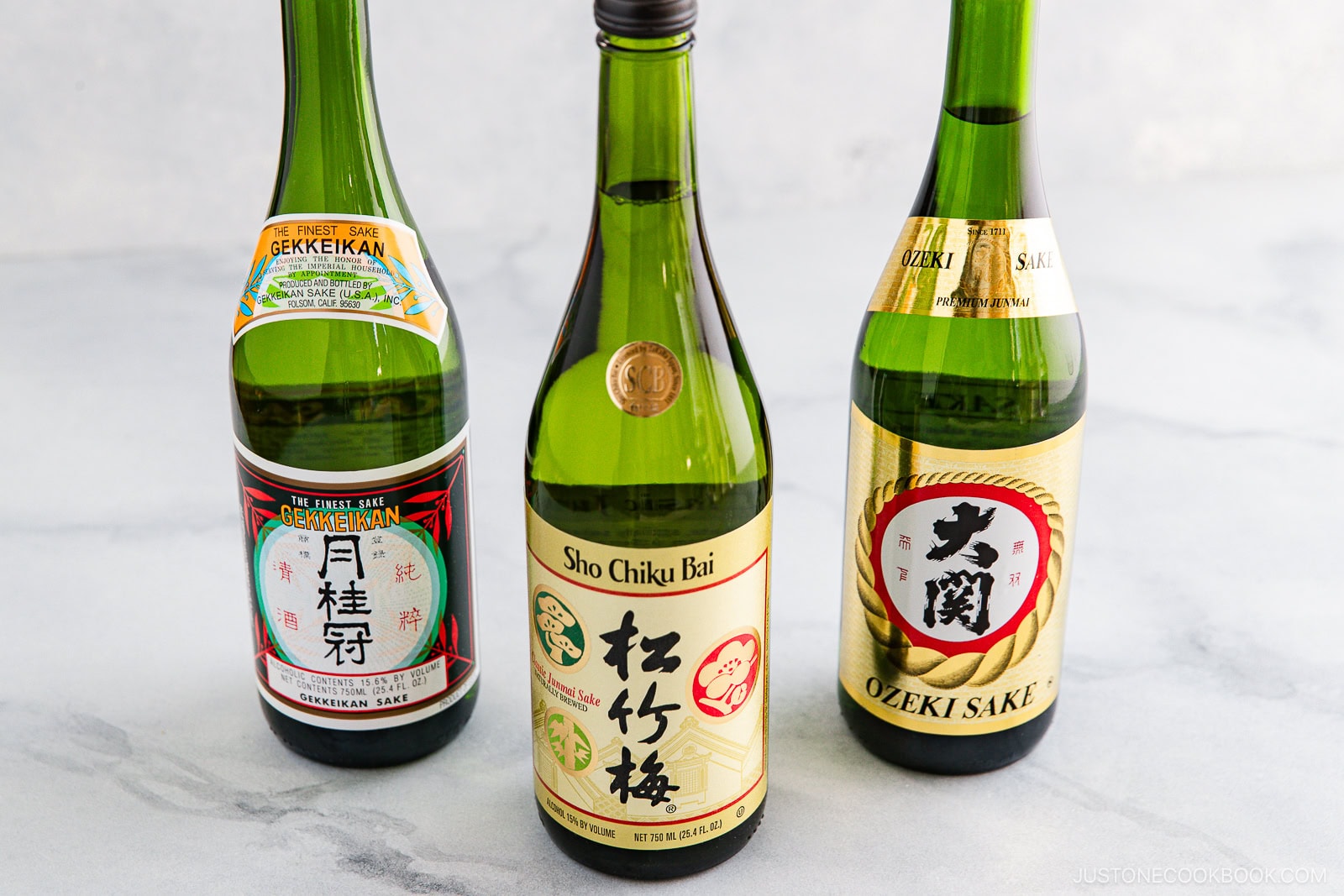 Three bottles of sake stand on a light gray surface, each with a unique label: Gekkeikan, Sho Chiku Bai, and Ozeki Sake—perfect for exploring Sake vs Mirin: Key Differences and How to Use Them in your cooking or tasting.